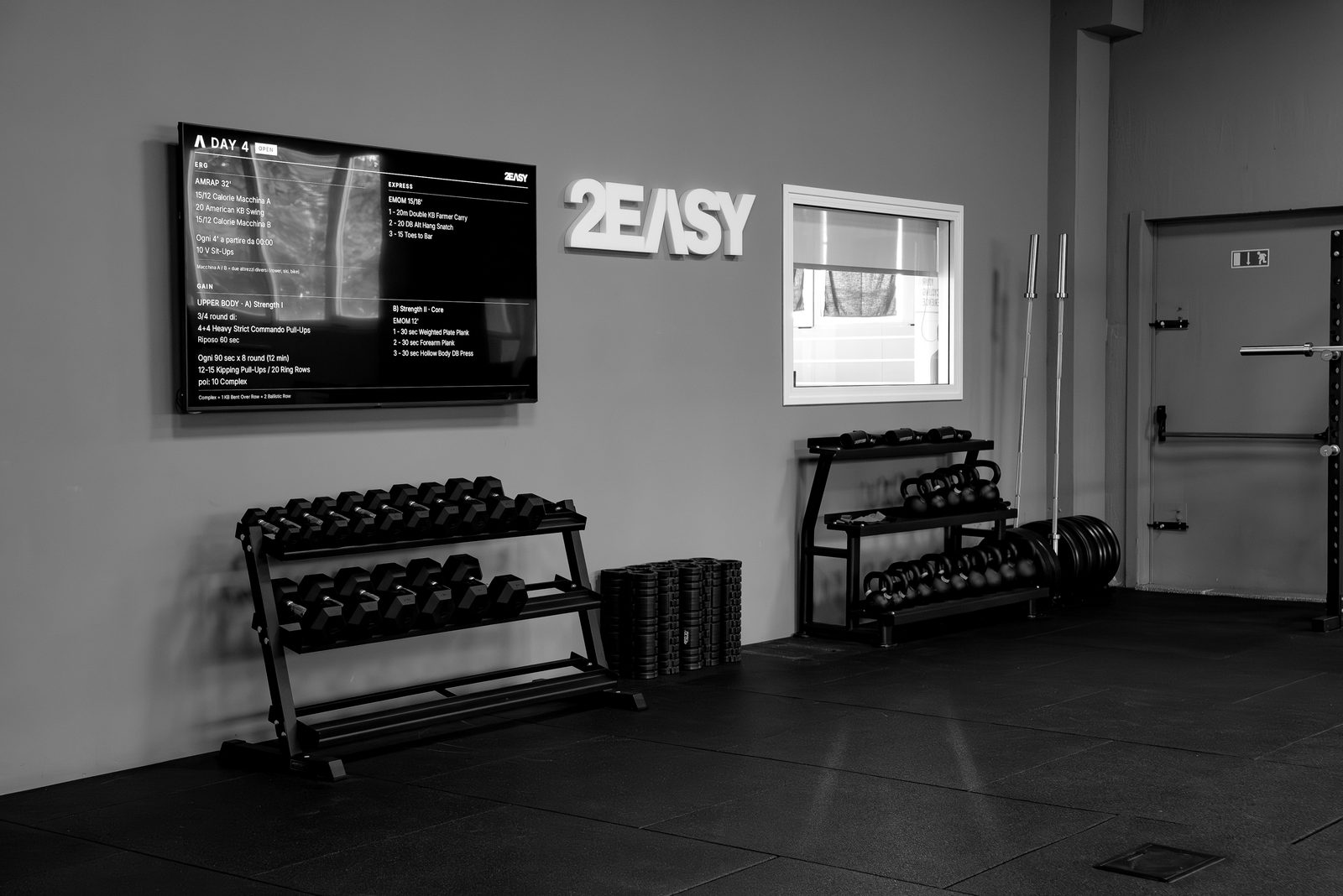 La sala funzionale di 2EASY con schermo dei workout e rastrelliere manubri e kettlebell